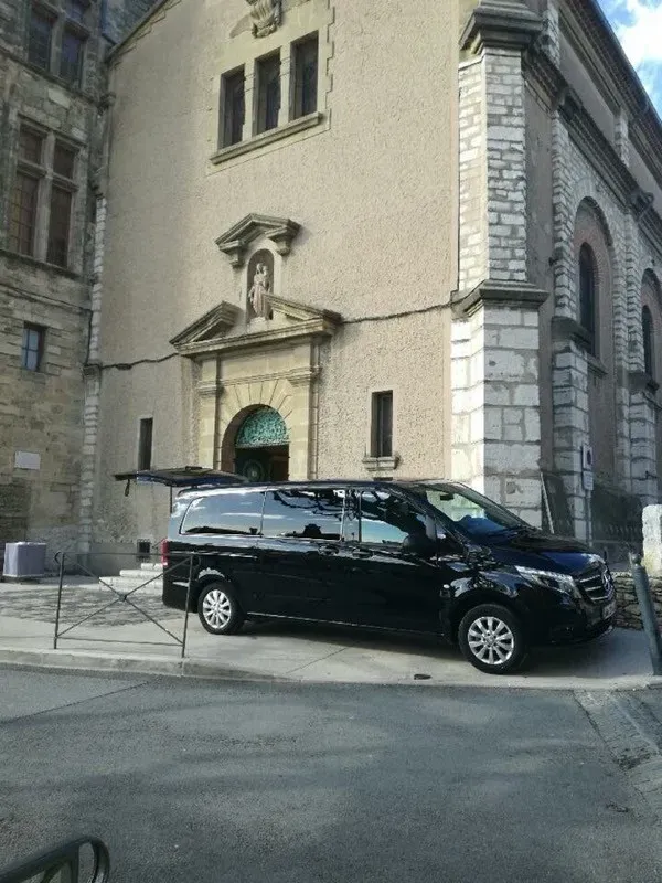 Véhicule funéraire noir Mercedes garé devant une église en pierre.