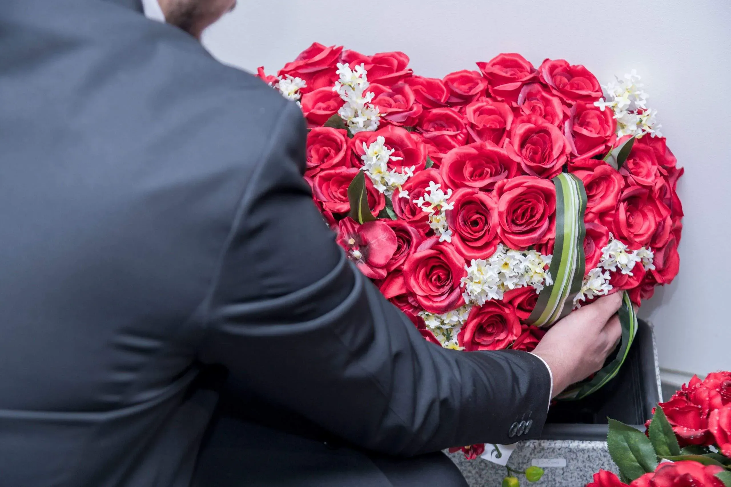 Agent funéraire disposant une composition florale en forme de cœur rouge.